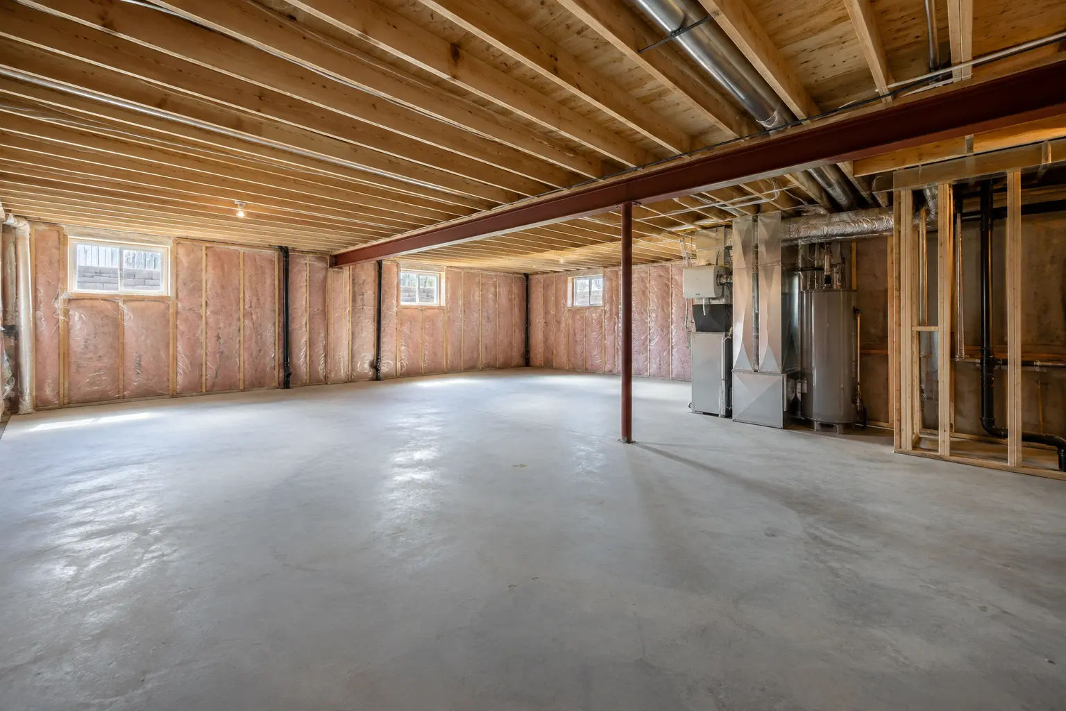 Wide unfinished basement with concrete floor, exposed joists and small windows.